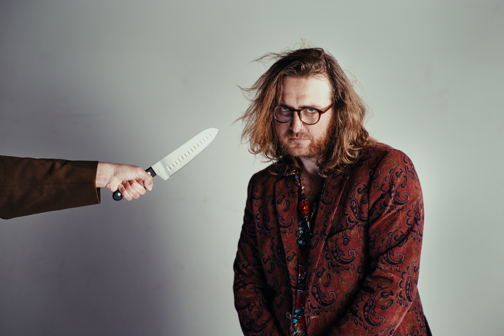 The Denim Emperor in a patterned red jacket beside an outstretched kitchen knife